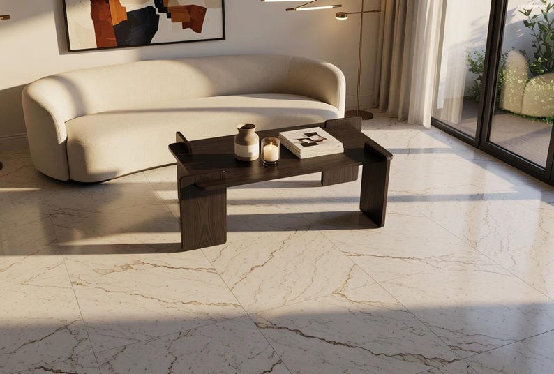 May include: A dark brown wooden coffee table with a rectangular top and two vertical side supports. On the table sits a small ceramic vase, a glass candle holder with a lit candle, and a white book. The table rests on a light marble floor.