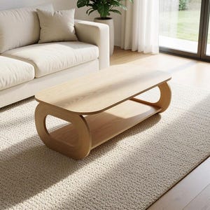 Puede incluir: Una mesa de centro de madera de tono claro con una superficie rectangular lisa de esquinas redondeadas y un estante inferior. La mesa se apoya en dos paneles laterales curvos y continuos que crean aberturas ovaladas en cada extremo.