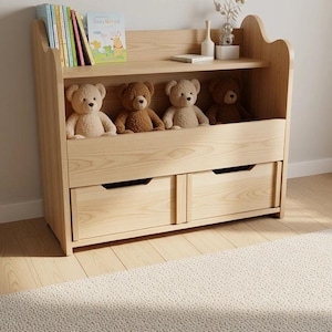 Op de afbeelding: Een speelgoedkast van licht hout met een open bovenplank voor kleurrijke boeken en kleine decoratieve items, een middengedeelte met vier pluche beren en twee onderste lades met uitgesneden handgrepen voor gemakkelijke toegang.