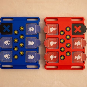 Peut inclure: Deux plateaux de jeu rectangulaires, un bleu et un rouge, chacun doté d'une grille de tuiles coulissantes. Le plateau bleu affiche des icônes de pieuvre blanches et un X noir, tandis que le rouge montre des scarabées et un X rouge. Des pions étoiles jaunes sont inclus.
