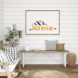 May include: A framed print with the text "WALK WITH ME" and a mountain graphic. The print is displayed above a wooden bench with pillows and a woven basket. The room has white shiplap walls and a wooden floor.