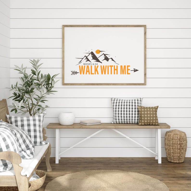 May include: A framed print with the text "WALK WITH ME" and a mountain graphic. The print is displayed above a wooden bench with pillows and a woven basket. The room has white shiplap walls and a wooden floor.