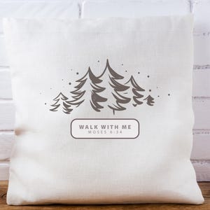 May include: A square, off-white pillow with a forest graphic. The design features several stylized pine trees in shades of gray, with small dots scattered around them. Below the trees is a rectangular box with the text "WALK WITH ME MOSES 6:34".