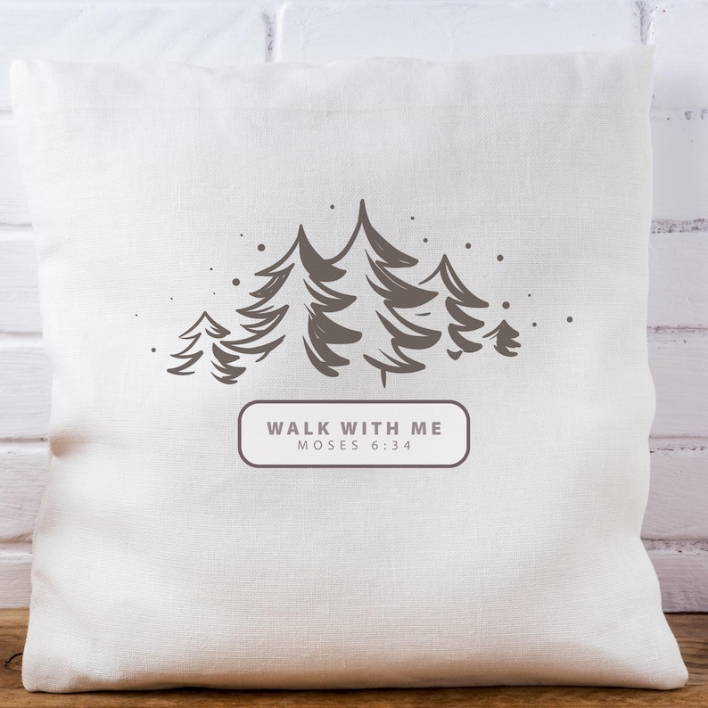 May include: A square, off-white pillow with a forest graphic. The design features several stylized pine trees in shades of gray, with small dots scattered around them. Below the trees is a rectangular box with the text "WALK WITH ME MOSES 6:34".