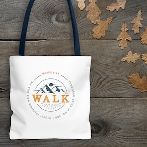 May include: White tote bag with navy blue handles featuring the word "WALK" in an orange and blue circular design with mountain graphics. The text "MOSES 6:34" is above the design, and other text surrounds the design.