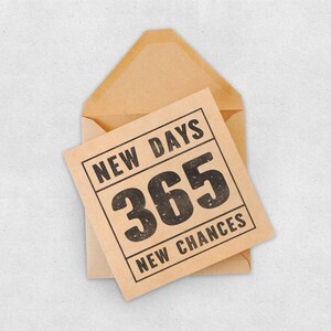 May include: A brown envelope with a card inside. The card is brown with black text that reads "NEW DAYS 365 NEW CHANCES".