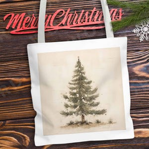K&ouml;nnte beinhalten: Eine wei&szlig;e Einkaufstasche mit einer Aquarell-Illustration eines gr&uuml;nen Weihnachtsbaums mit wei&szlig;en Ornamenten auf beigefarbenem Hintergrund.
