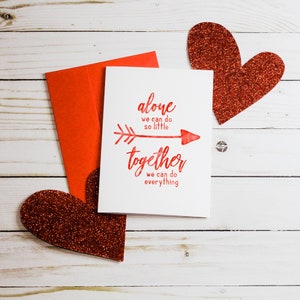 Puede incluir: Una tarjeta blanca con letras rojas que dice "alone we can do so little together we can do everything". La tarjeta tiene una flecha roja apuntando hacia la derecha. La tarjeta est&aacute; rodeada de dos corazones rojos de purpurina.