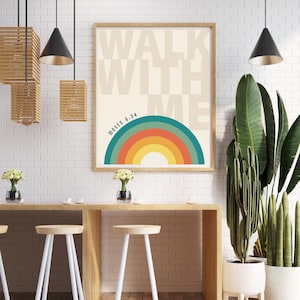 May include: A framed art print with the words "WALK WITH ME" in beige block letters. Below the text is a colorful rainbow design. The text "MOSES 6:34" is printed below the rainbow. The print is in a light brown wooden frame.