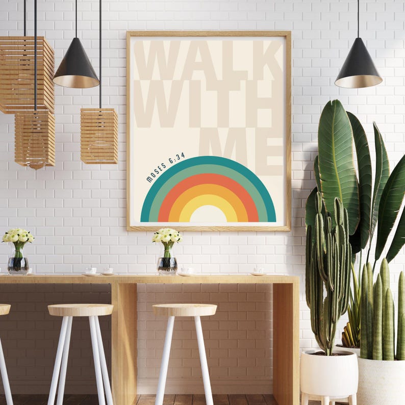 May include: A framed art print with the words "WALK WITH ME" in beige block letters. Below the text is a colorful rainbow design. The text "MOSES 6:34" is printed below the rainbow. The print is in a light brown wooden frame.