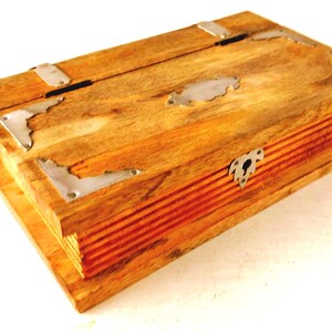 May include: Wooden box with a hinged lid and a decorative metal clasp. The box is made of light-colored wood with visible grain and metal corner accents. The box is rectangular and appears to be a storage container.
