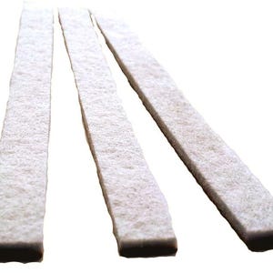May include: Three rectangular, off-white felt strips are arranged diagonally against a white background. The felt has a slightly textured appearance and a dark brown edge. The strips are evenly spaced and appear to be new.
