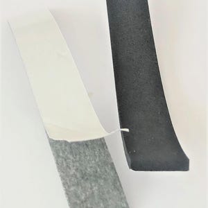 May include: Two pieces of black foam tape with adhesive backing. One piece has the white backing partially peeled away, revealing the gray adhesive. The other piece is solid black.