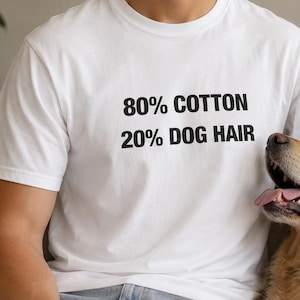 Peut inclure: Un t-shirt blanc à manches courtes avec le texte imprimé en noir 80% COTTON 20% DOG HAIR centré sur la poitrine. Le vêtement est associé à un jean bleu clair, créant un look décontracté qui met en valeur le design graphique humoristique.