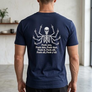 May include: A navy blue t-shirt featuring a white graphic on the back of a multi-armed skeleton giving the middle finger with every hand. Below the skeleton, the text reads: Fuck you, Fuck this, Fuck that, Fuck it, Fuck off, Fuck all, Fuck y'all.