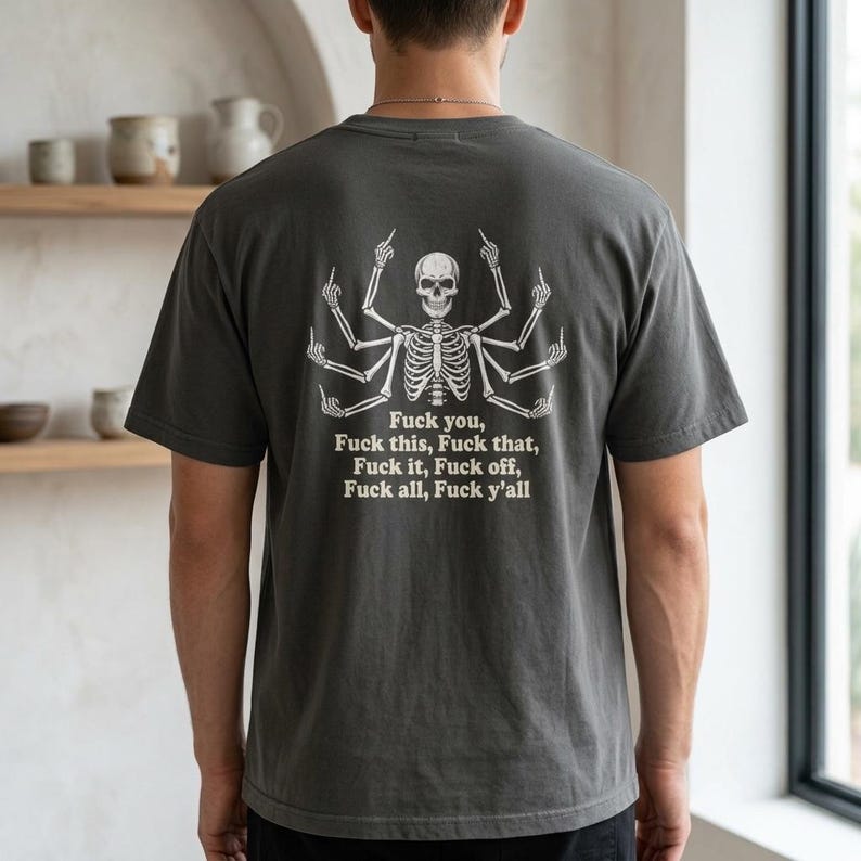 May include: A charcoal grey t-shirt featuring a white graphic on the back of a multi-armed skeleton giving the middle finger with every hand. Below the skeleton, the text reads: Fuck you, Fuck this, Fuck that, Fuck it, Fuck off, Fuck all, Fuck y'all.