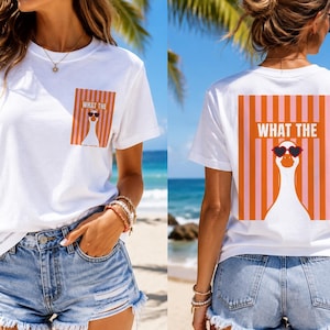May include: A white short-sleeve t-shirt featuring a graphic of a goose wearing heart-shaped sunglasses. The front pocket area and the back display the text WHAT THE above the goose, set against a background of vertical orange and pink stripes.