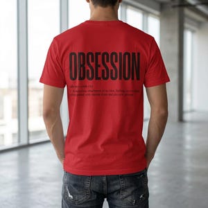 May include: A red short-sleeved t-shirt featuring the black text OBSESSION in a large font, followed by the definition: ob-session (n) 1. A relentless attachment to an idea, feeling, or emotion, often paired with mental strain and physical unease.
