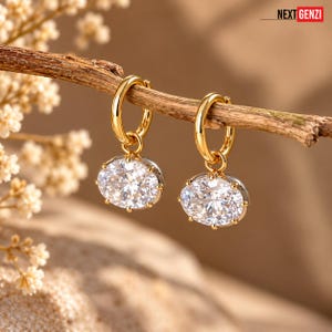 May include: A pair of gold hoop earrings with oval-shaped clear faceted stones hanging from each hoop. The earrings are suspended from a thin wooden branch. The text NEXT GENZI is visible in the upper right corner of the image.