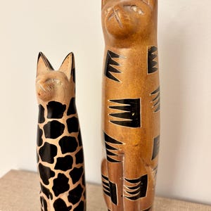 Par de estatuetas decorativas de gatos esculpidas em pedra-sabão nas cores marrom, creme e preto.