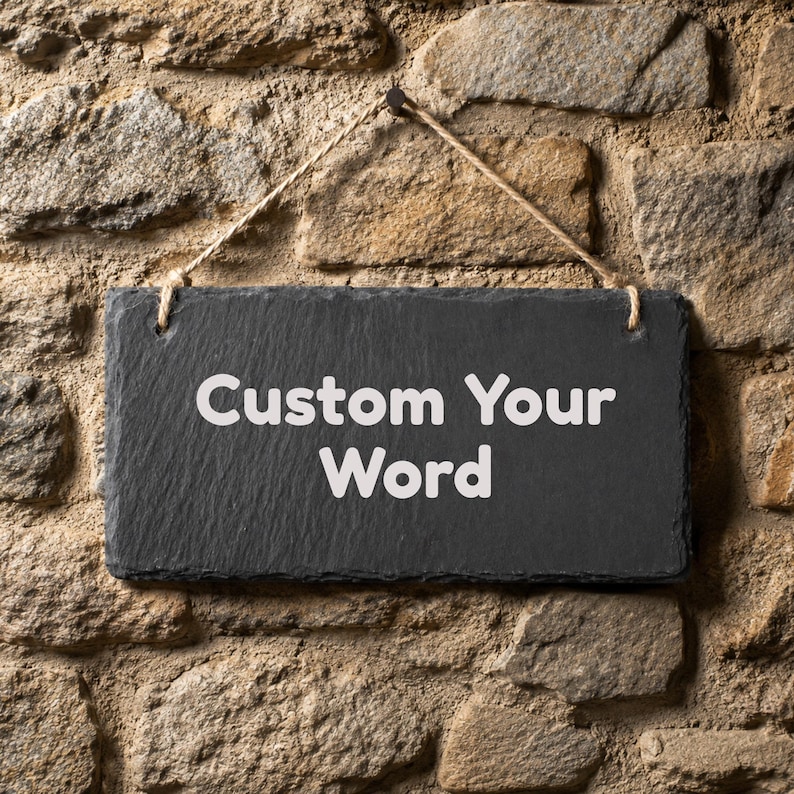 Puede incluir: Un letrero rectangular de pizarra negra con una superficie rugosa y texturizada de bordes irregulares. El letrero presenta el texto blanco "Custom Your Word" impreso en el centro y est&aacute; suspendido por una cuerda de yute marr&oacute;n claro.