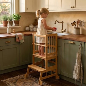 May include: A light-colored wooden kitchen learning tower with a safety rail and a step stool base. The structure is designed for children to reach kitchen counters safely, featuring a sturdy frame, vertical slats, and a natural wood finish.