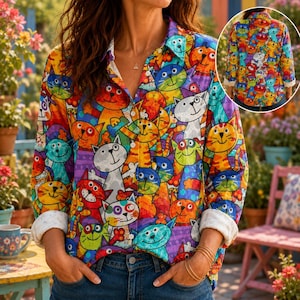 May include: A long-sleeved button-down shirt featuring a vibrant, multicolored pattern of cartoon cats in various colors including orange, blue, green, and purple. The shirt has a classic collar, a front button placket, and white cuffs.