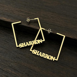May include: A pair of gold-toned square hoop earrings featuring the name SHARRON integrated into the bottom bar of each frame. The earrings have a thin, minimalist wire construction with standard post-back closures for secure attachment.