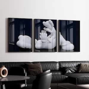 May include: A triptych of framed art prints featuring white cartoon-like figures with X-shaped eyes and hands. The figures are set against a dark blue background, with a black frame. The artwork is displayed above a black leather sofa.