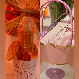 May include: A bottle of Lotus Petals B Silkwood Desire Pheromone Infused oil, with a gold cap and a label. The bottle is wrapped in cellophane and tied with a bow. A pink gift bag with a thank you note is also visible.