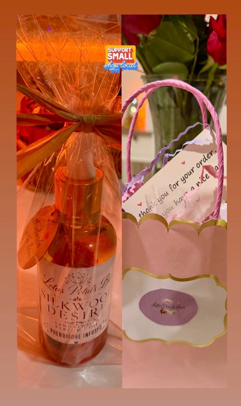May include: A bottle of Lotus Petals B Silkwood Desire Pheromone Infused oil, with a gold cap and a label. The bottle is wrapped in cellophane and tied with a bow. A pink gift bag with a thank you note is also visible.