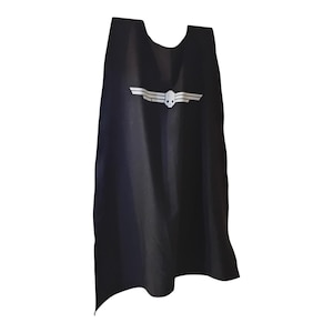 Pode incluir: Capa preta com um desenho de caveira e asas brancas. A capa é feita de um tecido escuro e tem um decote arredondado. O gráfico branco está centrado na frente.