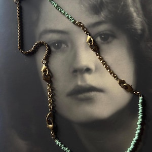 May include: A necklace featuring a combination of gold-toned metal chain links and small, light turquoise beads. The design incorporates multiple lobster claw clasps integrated into the chain structure, with a single white, irregular pearl accent.