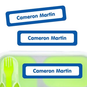 May include: Three blue and white rectangular labels with the text "Cameron Martin". One label is affixed to a green and white lunchbox with a lime green fork and spoon. The labels are for personal organization.