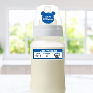 May include: A clear baby bottle with a white cap and two blue labels. The top label is bear-shaped with the text Liam Williams. The rectangular bottom label displays the name Liam Williams, the date 9/18, 6 ounces, and Breast Milk.