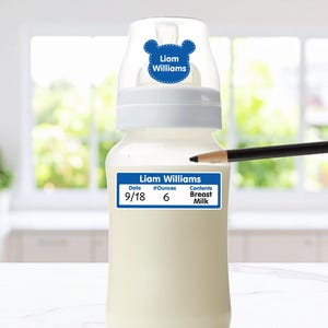 May include: A baby bottle with a white cap featuring a blue bear-shaped label with the text Liam Williams. A rectangular blue label on the bottle displays the text Liam Williams, Date 9/18, #Ounces 6, and Contents Breast Milk.