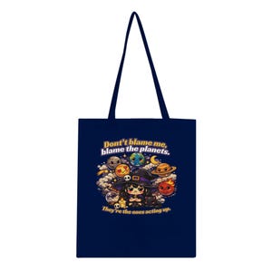 May include: A navy blue tote bag with a colourful illustration of a witch and planets, and the text "Don't blame me, blame the planets. They're the ones acting up." The bag has long handles for carrying.