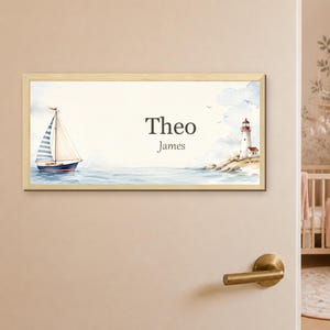 May include: A rectangular wooden-framed wall sign featuring a watercolour illustration of a sailboat on the left and a lighthouse on the right. The centre displays the text Theo James in a dark grey serif font against a light cream background.
