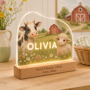 May include: An illuminated acrylic night light featuring a printed scene of a cow and a sheep in a field with a red barn. The name OLIVIA is printed in white in the center. The wooden base is engraved with the text Sweet Dreams, Olivia Love, Mom.