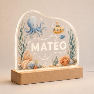 May include: An illuminated acrylic night light featuring a printed underwater scene with a blue octopus, a yellow submarine, sea plants, shells, and a starfish. The name MATEO is printed in white capital letters in the center of the display.