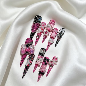 May include: A set of long, pointed artificial nails in various designs. The nails feature a combination of black, pink, and white colors, with embellishments like rhinestones, bows, and cartoon character designs. Some nails have a tiger stripe pattern.