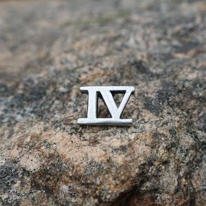 May include: A silver Roman numeral four charm, IV, on a rough, gray rock.