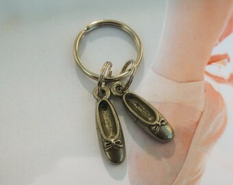 Puede incluir: Llavero de plata con dos dijes de zapato de bailarina de plata. Los dijes están detallados con un lazo en la punta de cada zapato.