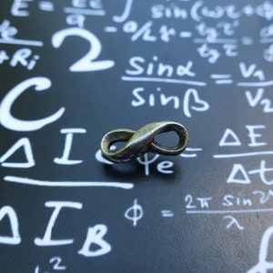 May include: A silver infinity symbol charm on a black background with white mathematical equations written on it. The equations include the symbols delta, phi, and omega.