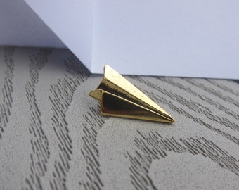 Könnte beinhalten: Ein goldfarbener Papierflieger-Anhänger. Der Anhänger ist aus Metall und hat ein realistisches Papierflieger-Design.