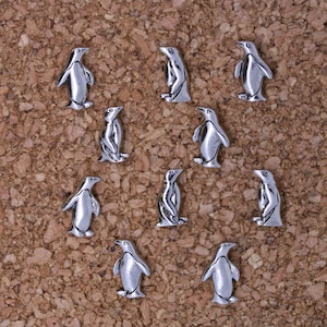 Könnte beinhalten: Eine Korktafel mit neun silbernen Pinguin-Reißnägeln, die in Herzform angeordnet sind.