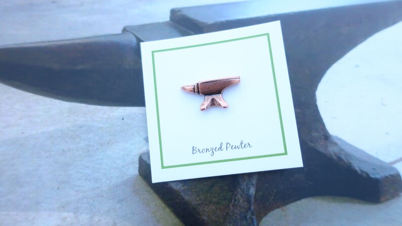 May include: A small, bronze-colored pewter anvil pin on a white card with green trim. The card reads "Bronzed Pewter".