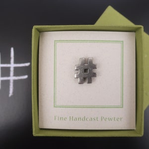 May include: A silver pewter hashtag charm in a green box with the text "Fine Handcast Pewter".