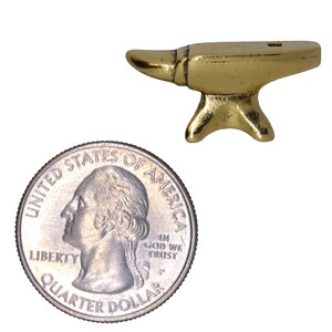 May include: A small gold-colored metal anvil, about the size of a US quarter. The anvil has a flat top and a rounded horn on one side.