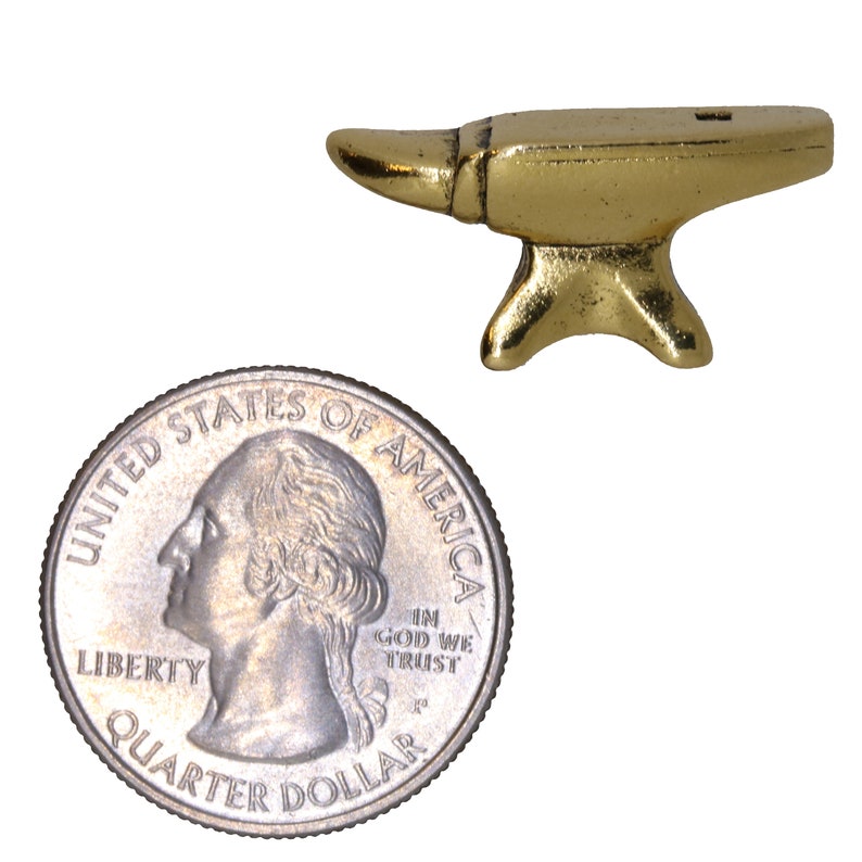 May include: A small gold-colored metal anvil, about the size of a US quarter. The anvil has a flat top and a rounded horn on one side.